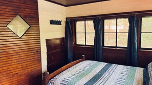 Une chambre à coucher avec une tête de lit en bois, un lit recouvert d’une couvre-lit à rayures, une table de chevet et une fenêtre avec des rideaux.