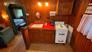 A compact kitchen with wooden walls, a red countertop, a white stove, and a coffee maker.