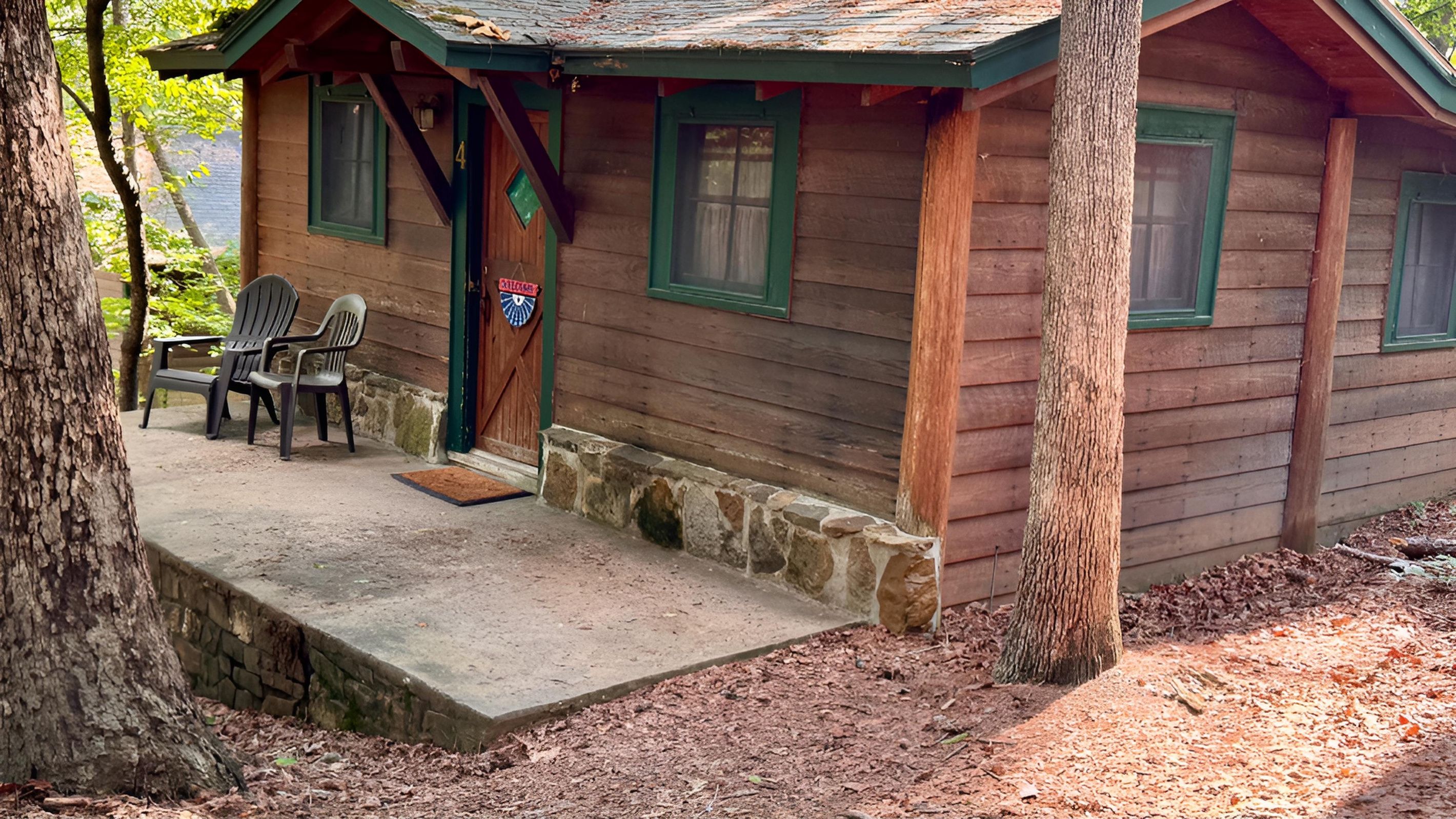 A wooden cabin with a porch, two chairs, and a stone foundation.