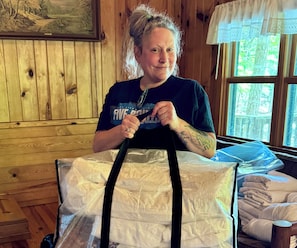 Eine Person hält ein großes, verpacktes Geschenk in einem Raum mit Holzwänden und einem Fenster.