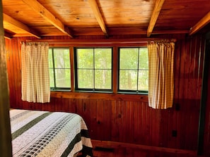 Ein Zimmer einer Holzhütte mit einem Bett, zwei Fenstern und Vorhängen.