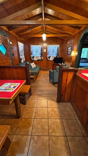 A wooden cabin interior with a dining area, seating, and a television.
