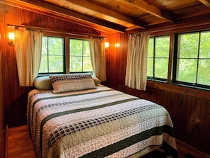 Ein Schlafzimmer einer Holzhütte mit einem Bett, Vorhängen und Fenstern.