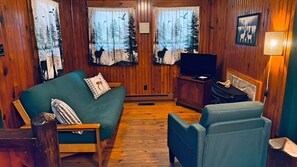 Interior acogedor de una cabaña con piso de madera, un sofá, un sillón, un televisor y una chimenea.