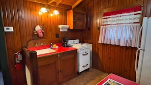 Eine kleine Küche mit Holzwänden, einer roten Arbeitsplatte, einem weißen Herd und einem Kühlschrank.