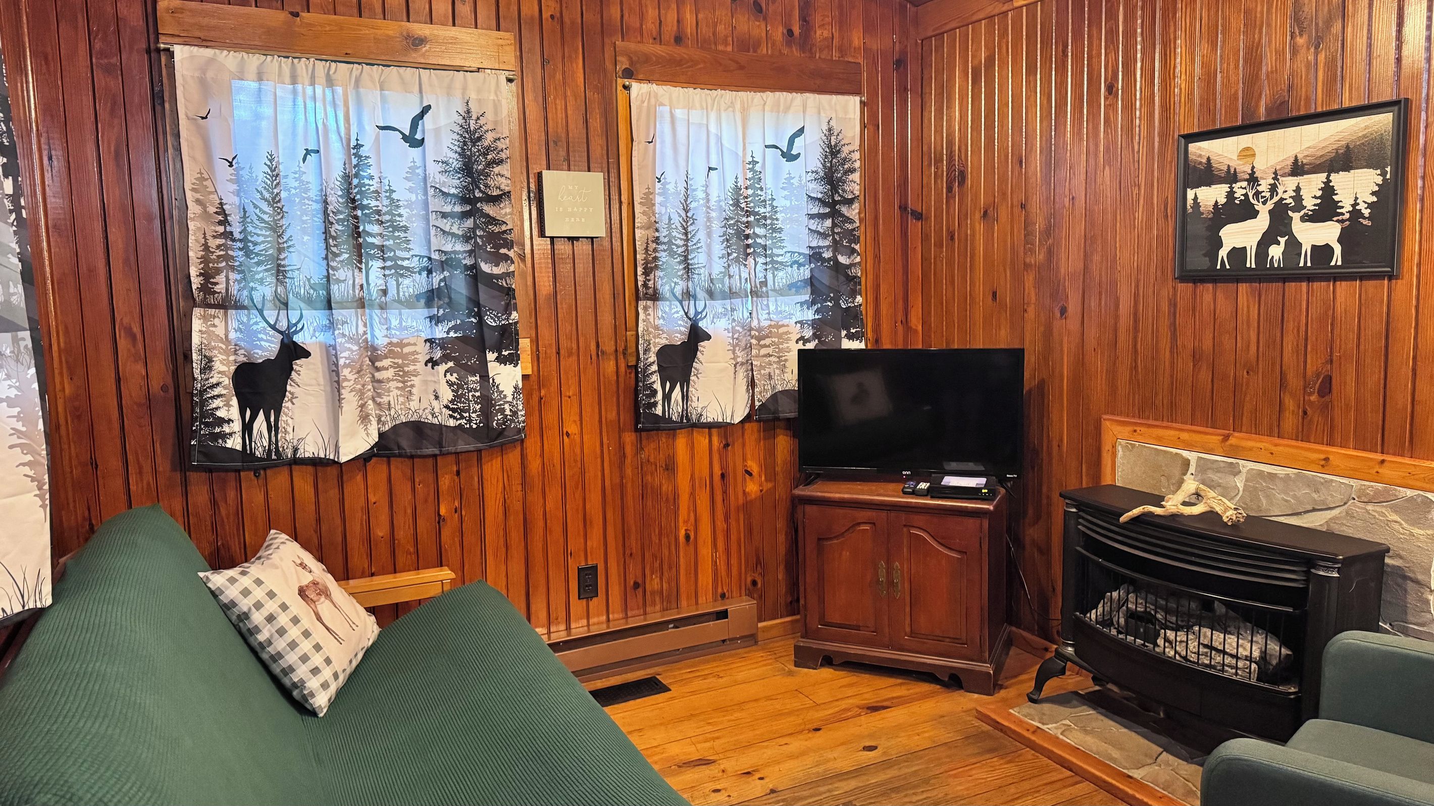 Tunnelmallinen mökin sisustus, jossa on puuseinät, vihreä sohva, televisio ja takka.