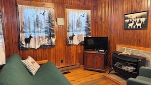Ein gemütliches Blockhaus-Interieur mit Holzwänden, einem grünen Sofa, einem Fernseher und einem Kamin.