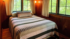 Un dormitorio de cabaña de madera con una cama, cortinas y ventanas.