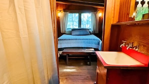 Interior de una cabaña de madera con una cama, un lavabo y una ventana.