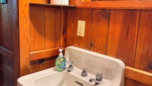 A bathroom with a white sink, two faucets, and a soap dispenser.