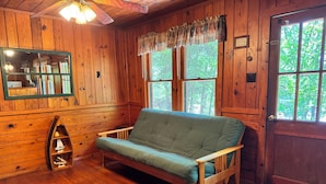 A wooden cabin interior with a green sofa, a wooden boat shelf, and a door with a window.