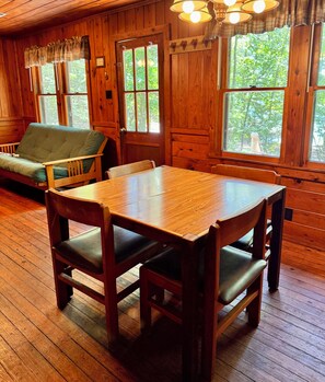Ein Holzinterieur mit Esstisch, Stühlen, einer Couch und großen Fenstern.
