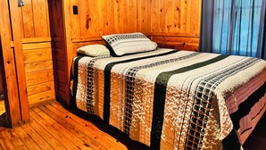 A wooden-paneled room with a bed, a wardrobe, and a window with curtains.