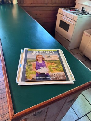 Una encimera de cocina con una revista titulada 'HOT SPRINGS DIAMOND LAKES VACATION GUIDE' que muestra una fotografía de una persona sosteniendo hielo.