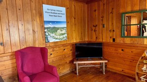 Ein Zimmer aus Holz mit einem Poster, einem roten Stuhl, einem kleinen Tisch mit einem Fernseher und einem Holzschrank.