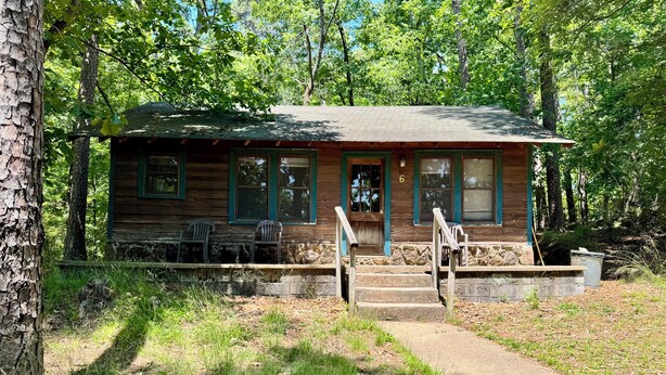 A rustic cabin with a porch, wooden steps, and two chairs.