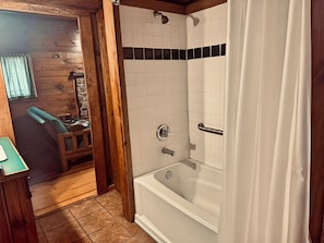 Un bagno con una vasca, una doccia e una porta in legno che dà su un soggiorno.