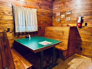 Interno di una baita in legno con tavolo da biliardo, panche di legno, estintore e quadri appesi al muro.