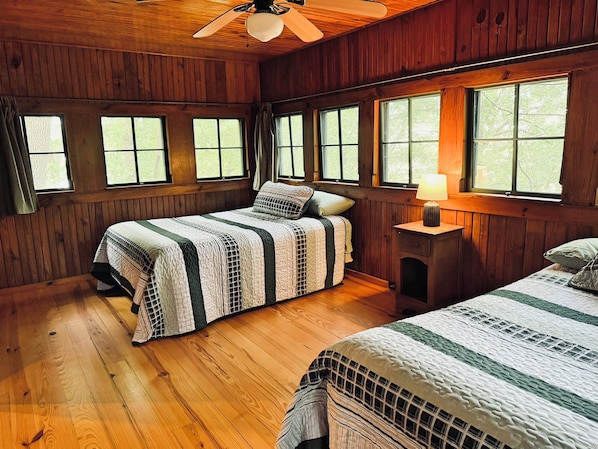 Un dormitorio tipo cabaña con una cama, una mesita de noche y una ventana.
