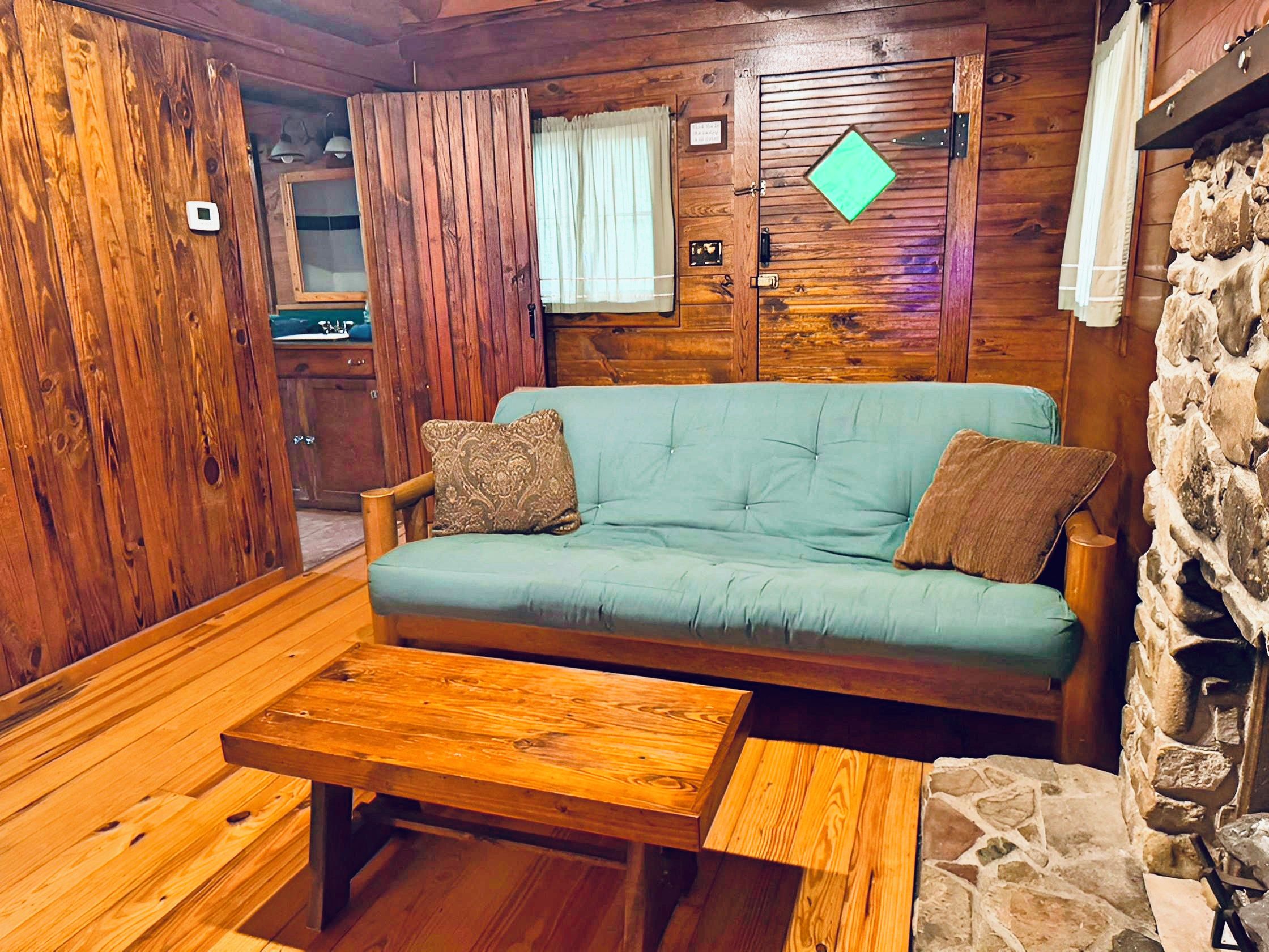 A cozy cabin interior with a wooden sofa, a small wooden table, and a stone wall.