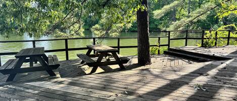 Une terrasse en bois avec des tables de pique-nique, donnant sur une étendue d’eau.