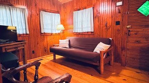 Un interior de madera con un sofá, un televisor sobre un mueble bajo y una silla.