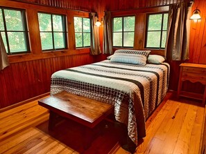 A wooden-paneled room with a bed, bench, and a small table.