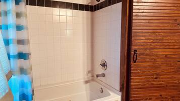 A bathroom with a bathtub, a shower, and a wooden door.