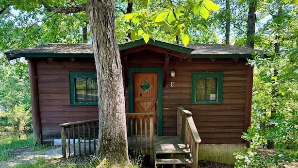 Ein rustikales Blockhaus mit Holztür, einer kleinen Veranda und einer Treppe, die zum Eingang führt.