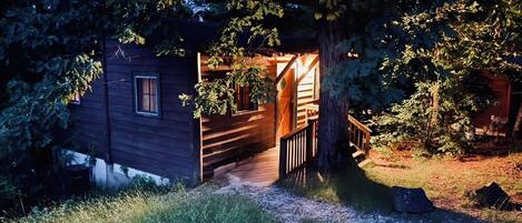 A wooden cabin with a wooden deck and a window, surrounded by trees and grass.