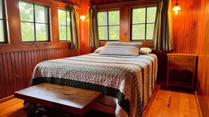 A wooden room with a bed, a bench, and a nightstand.