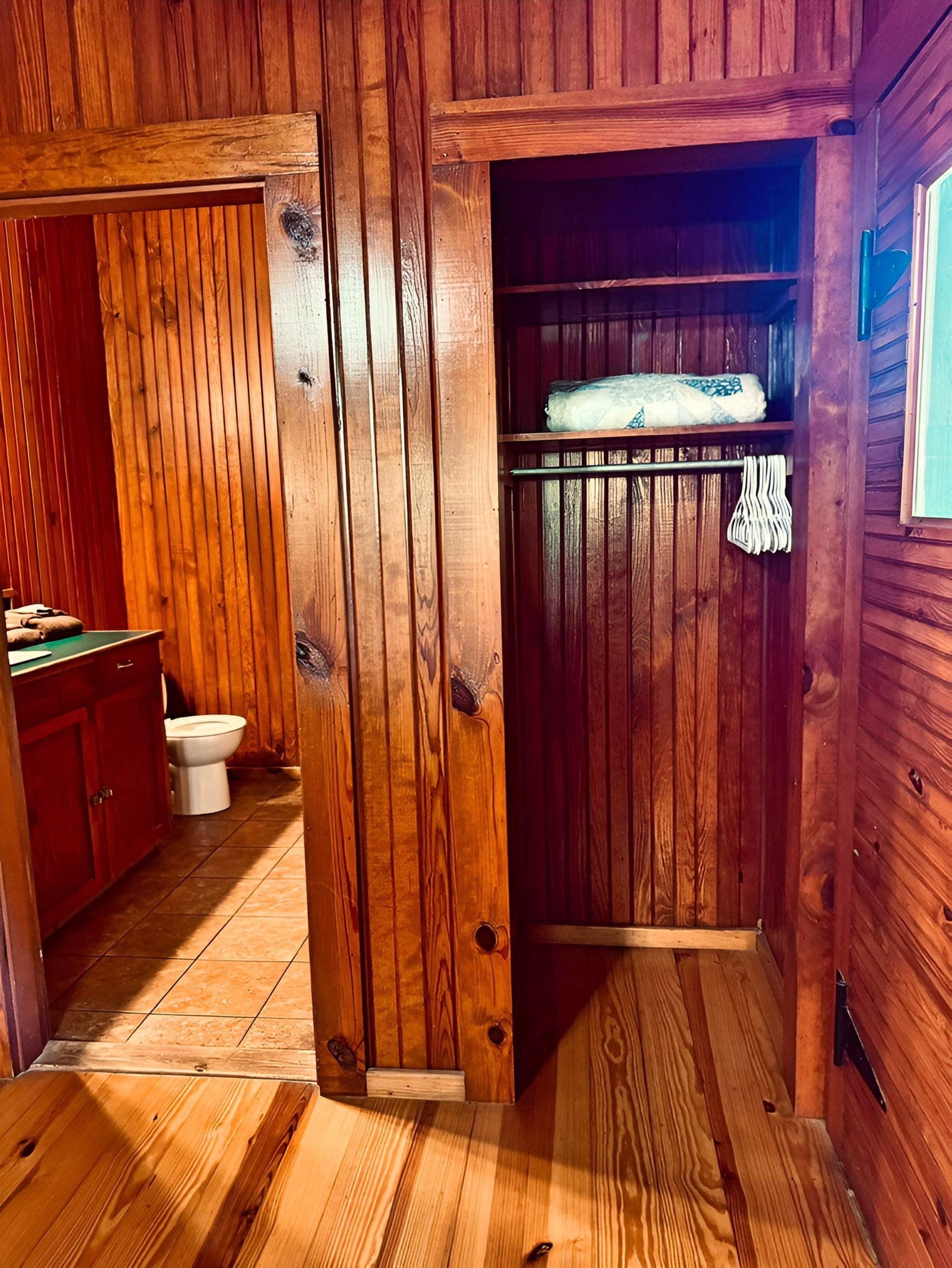 A wooden interior with a wooden door, a toilet, and a small shelf with a towel.