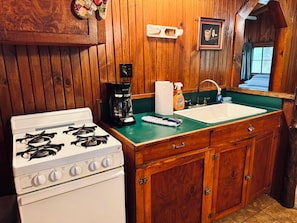 Una cocina con estufa blanca, armarios de madera, encimera verde, cafetera y fregadero.