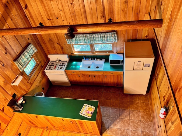 Une cuisine compacte avec des murs en bois, une cuisinière, un four à micro-ondes, un évier et un réfrigérateur.