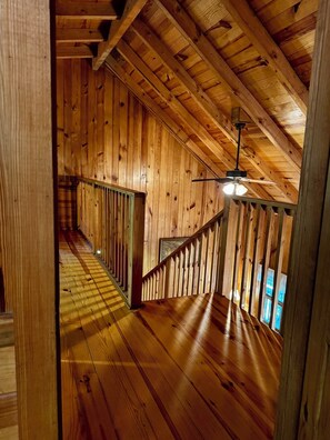 Un interior de madera con techo inclinado, una escalera y un ventilador de techo.