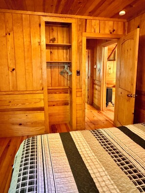 Interior de una cabaña de madera con una cama, un armario de madera y una puerta que da a otra habitación.