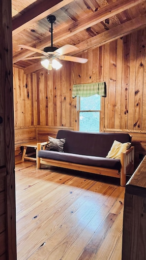 A wooden interior with a sofa, a ceiling fan, and a window.