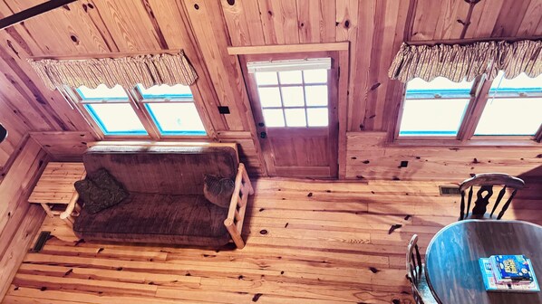 A wooden cabin interior with a sofa, a table, and two windows with curtains.