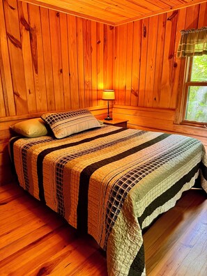 Una habitación con paneles de madera, una cama, una mesita de noche y una ventana.