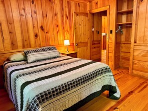 Une pièce aux murs lambrissés, comprenant un lit, une table de chevet et une armoire en bois.