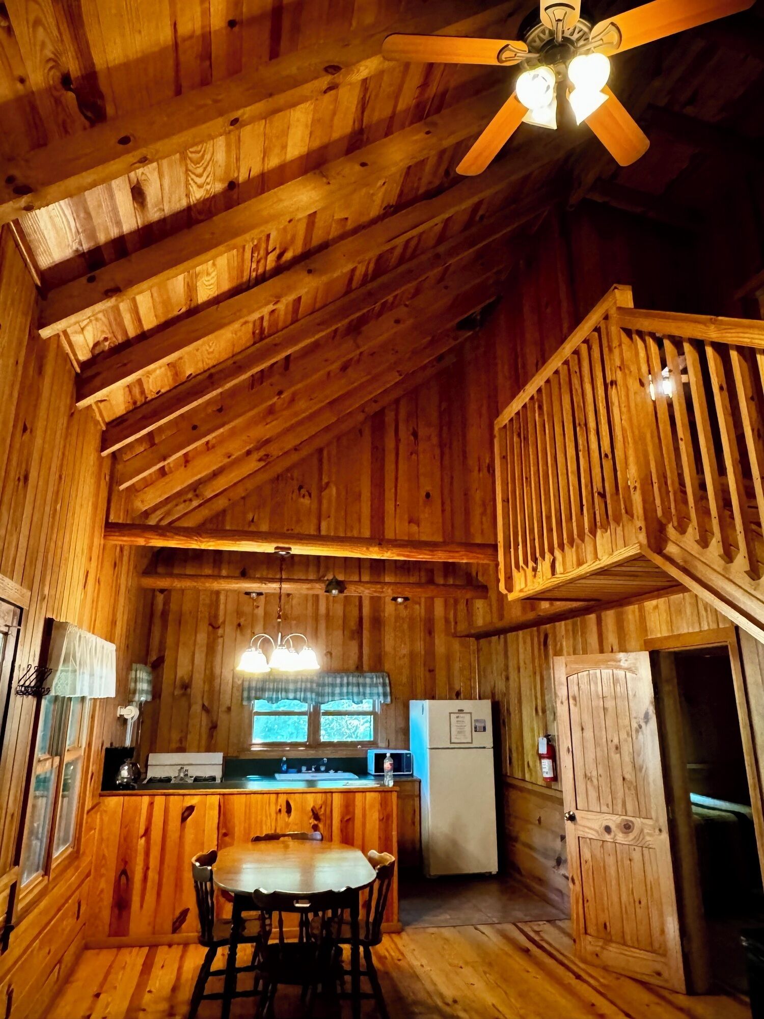 Interior de una cabaña de madera con cocina, comedor y balcón.