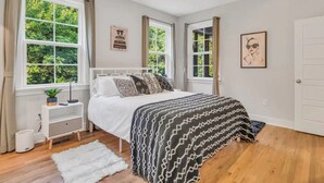 Un dormitorio con cama, mesita de noche, ventana y puerta.