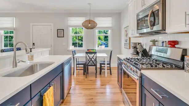 Una cocina moderna con armarios blancos, una isla grande, electrodomésticos de acero inoxidable y un comedor con mesa y sillas.