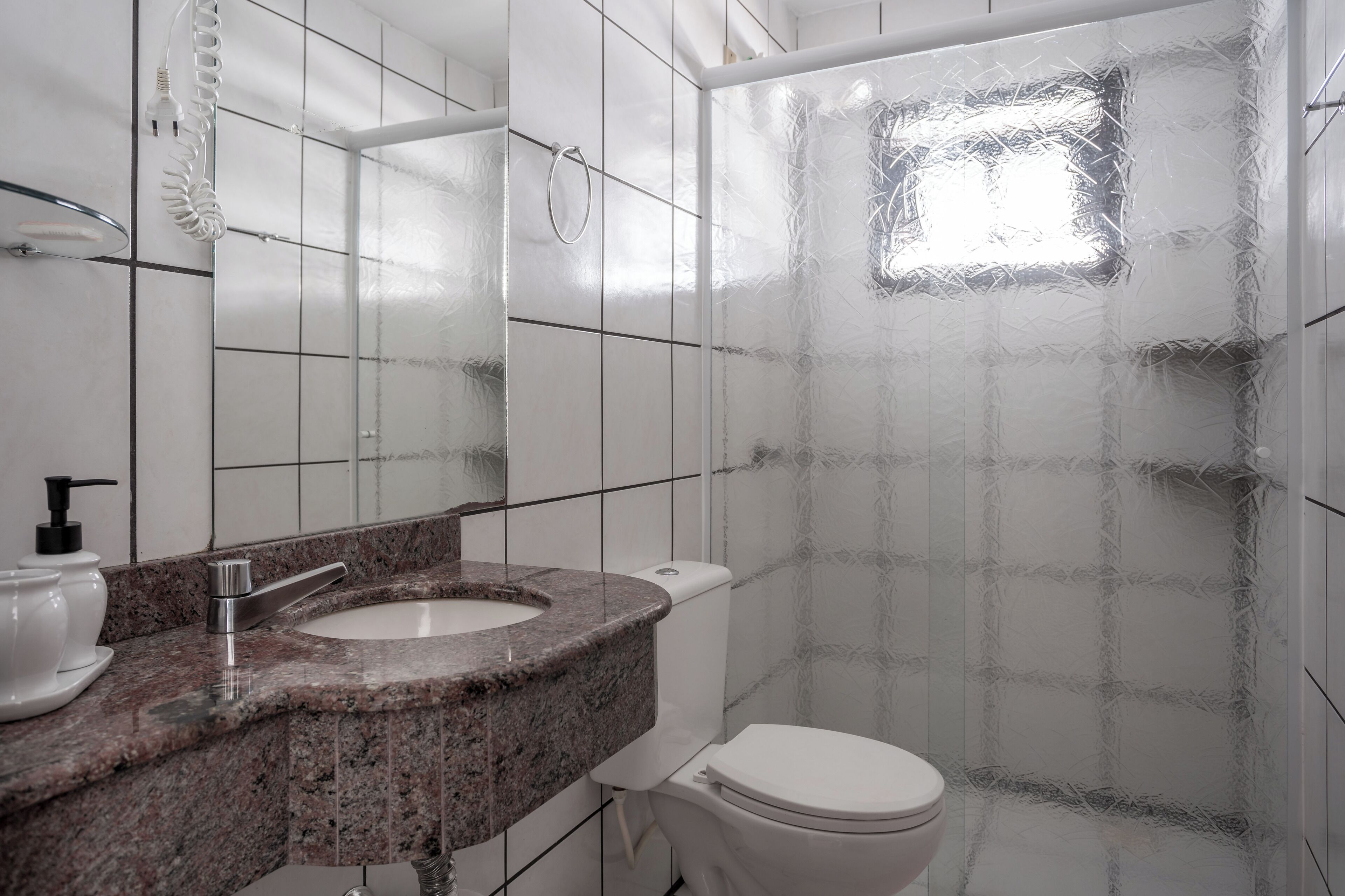 Une salle de bain avec un lavabo sur un plan de toilette en granit, des toilettes blanches et une douche aux parois en verre dépoli.