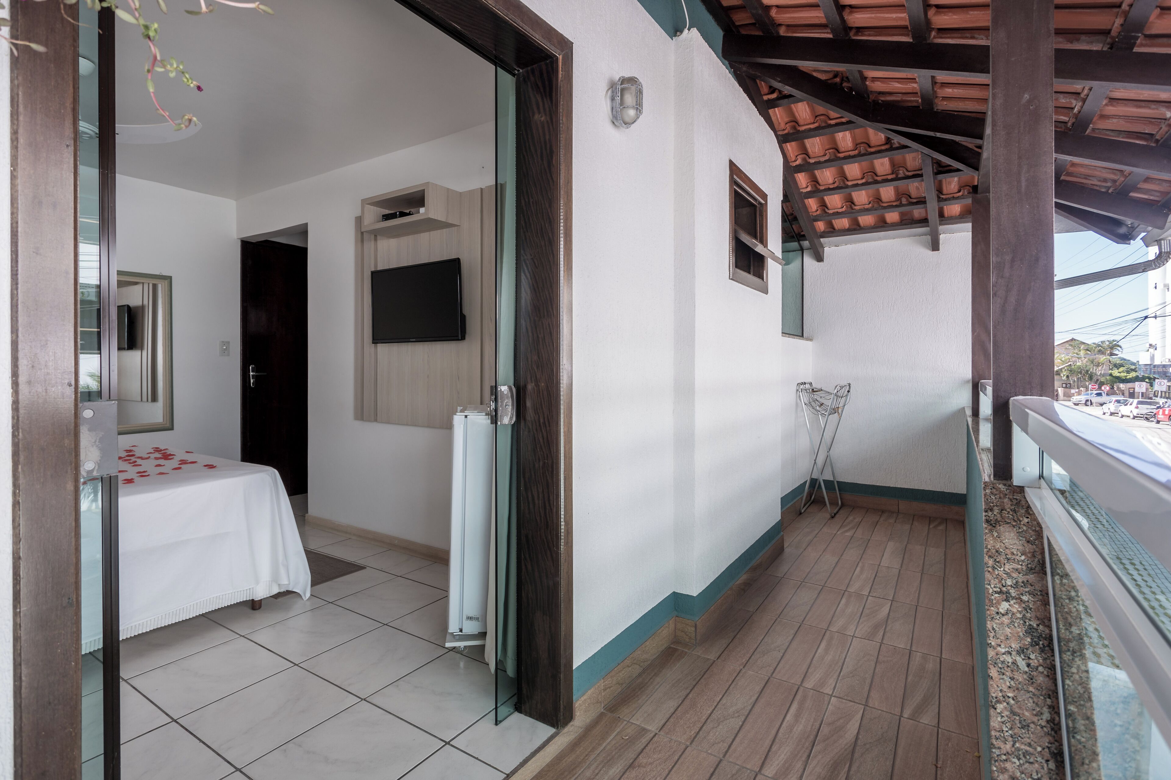 Una habitación con cama, televisión y balcón con vista a la calle.