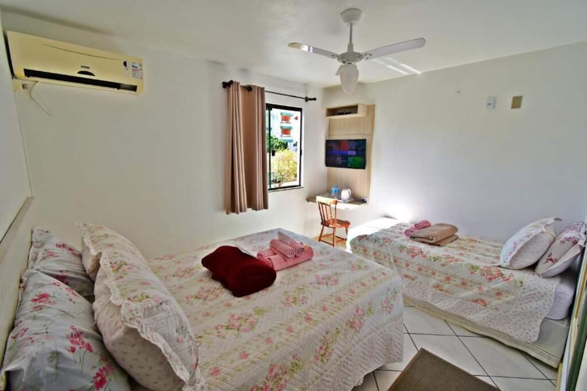 A hotel room with two beds, a ceiling fan, an air conditioning unit, a TV, and a window with curtains.