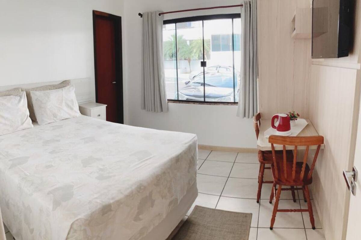 A bedroom with a bed, a desk, a chair, a window, and a television.