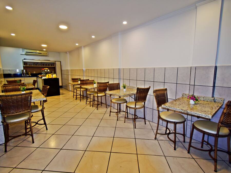 A restaurant with multiple tables and wicker chairs, a kitchen in the background, and tiled walls.