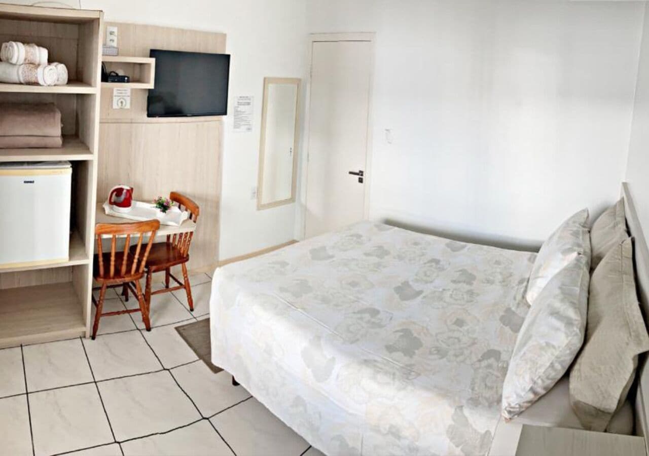 A bedroom with a bed, a desk with a chair, a television, and a wardrobe.