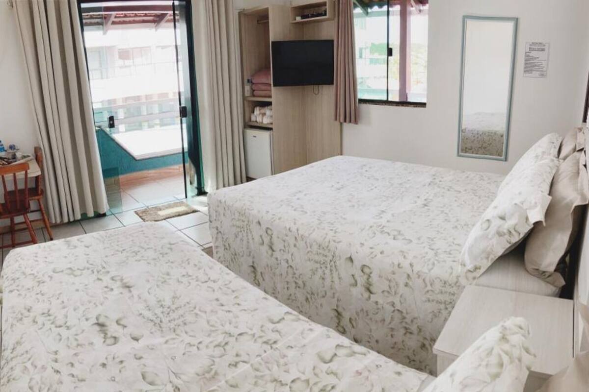 A hotel room with two beds, a TV, a small desk, and a view of the outside.